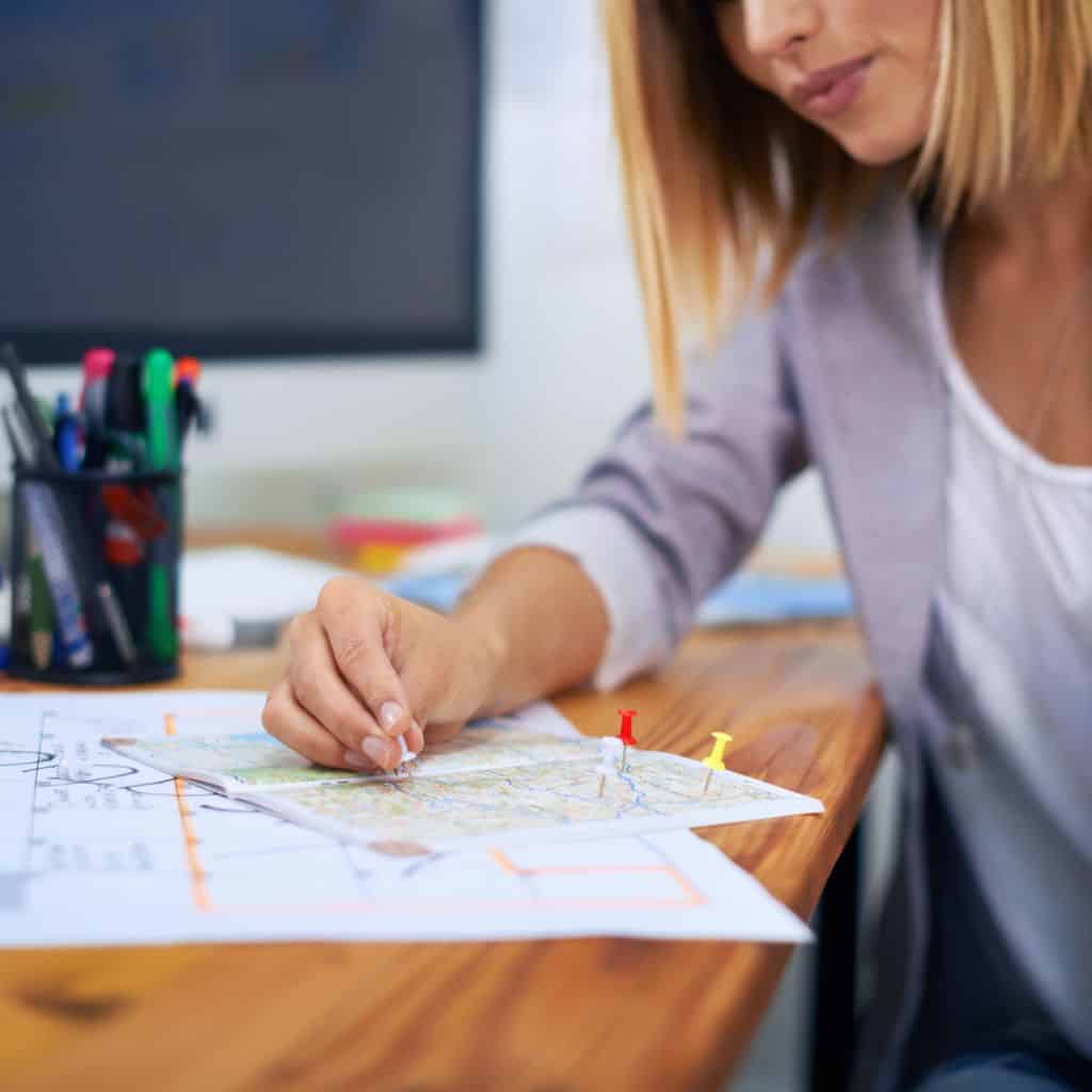 Travel agent sitting at her desk adding push pins to a map while planning a vacation.
